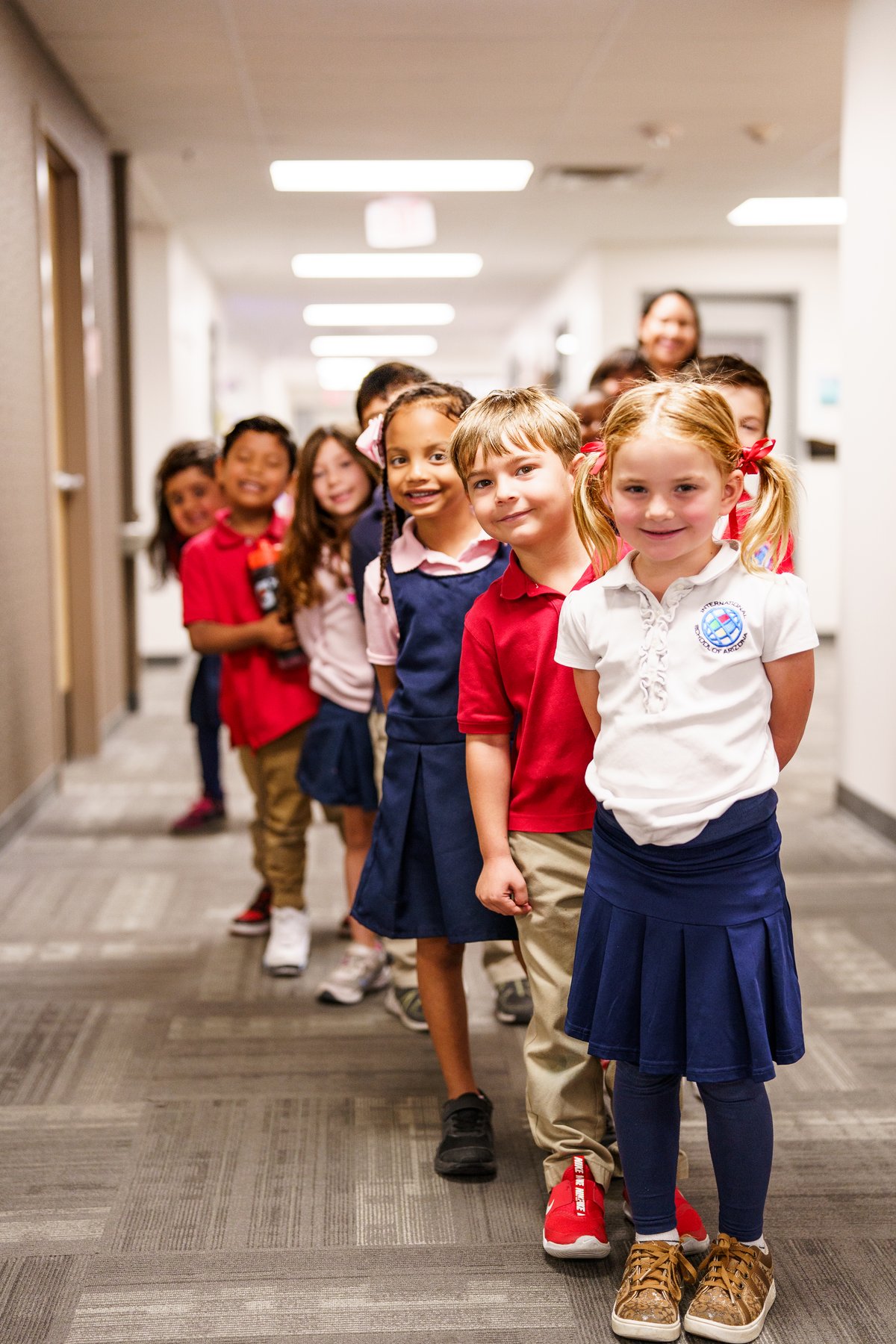  Group of young students in school uniforms smiling in a hallway at the International School of Arizona.
